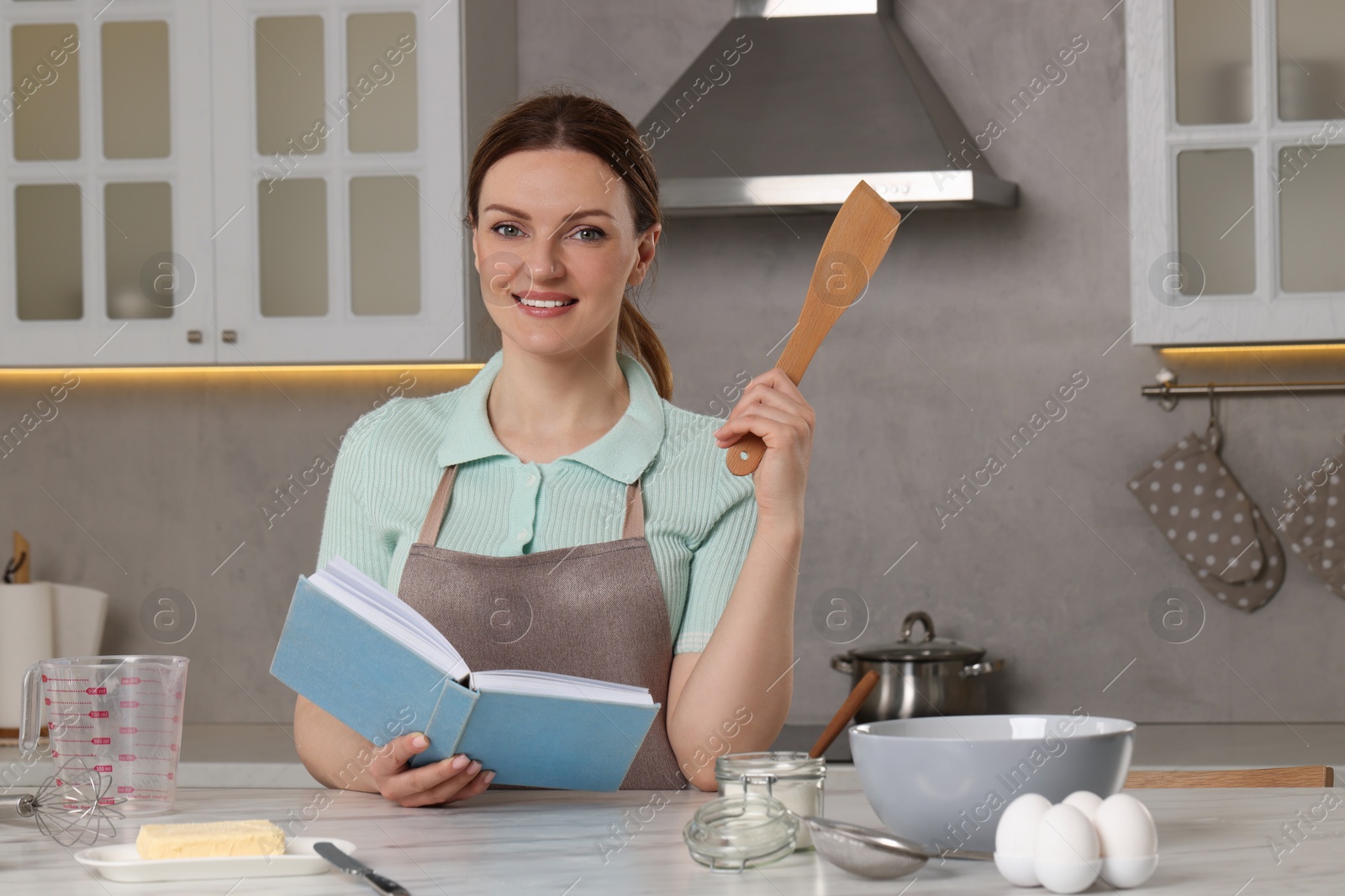 Photo of Happy woman with recipe book at white marble table in kitchen