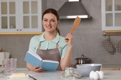 Photo of Happy woman with recipe book at white marble table in kitchen