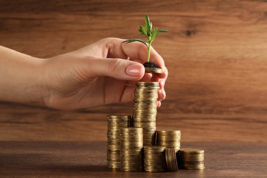 Photo of Woman putting coin onto stack with green sprout at wooden table, closeup. Investment concept