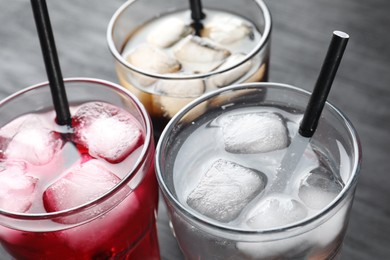 Photo of Glasses of different refreshing soda water with ice cubes and straws on grey table, closeup