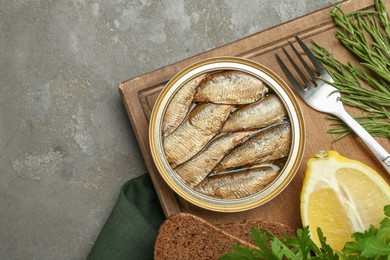 Photo of Tin can with tasty sprats served on grey textured table, flat lay. Space for text