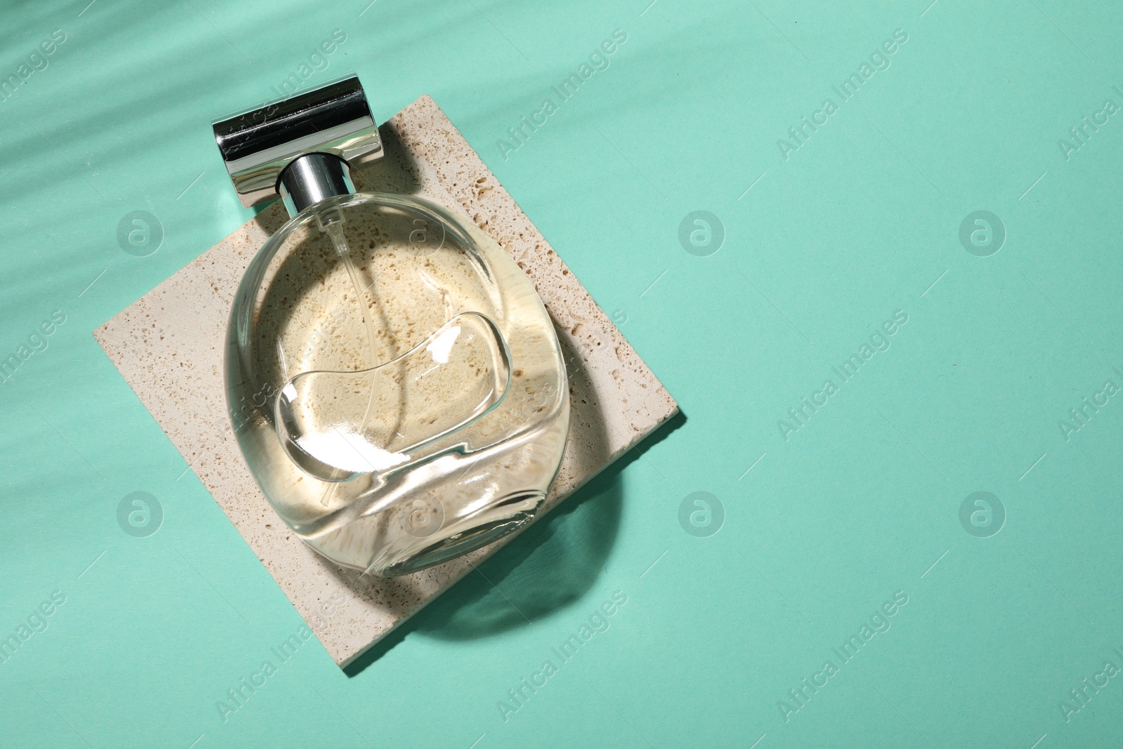 Photo of Bottle of luxury perfume in sunlight on turquoise background, top view. Space for text