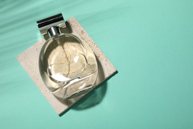 Bottle of luxury perfume in sunlight on turquoise background, top view. Space for text