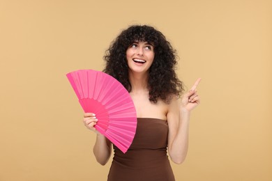 Happy woman holding hand fan on beige background