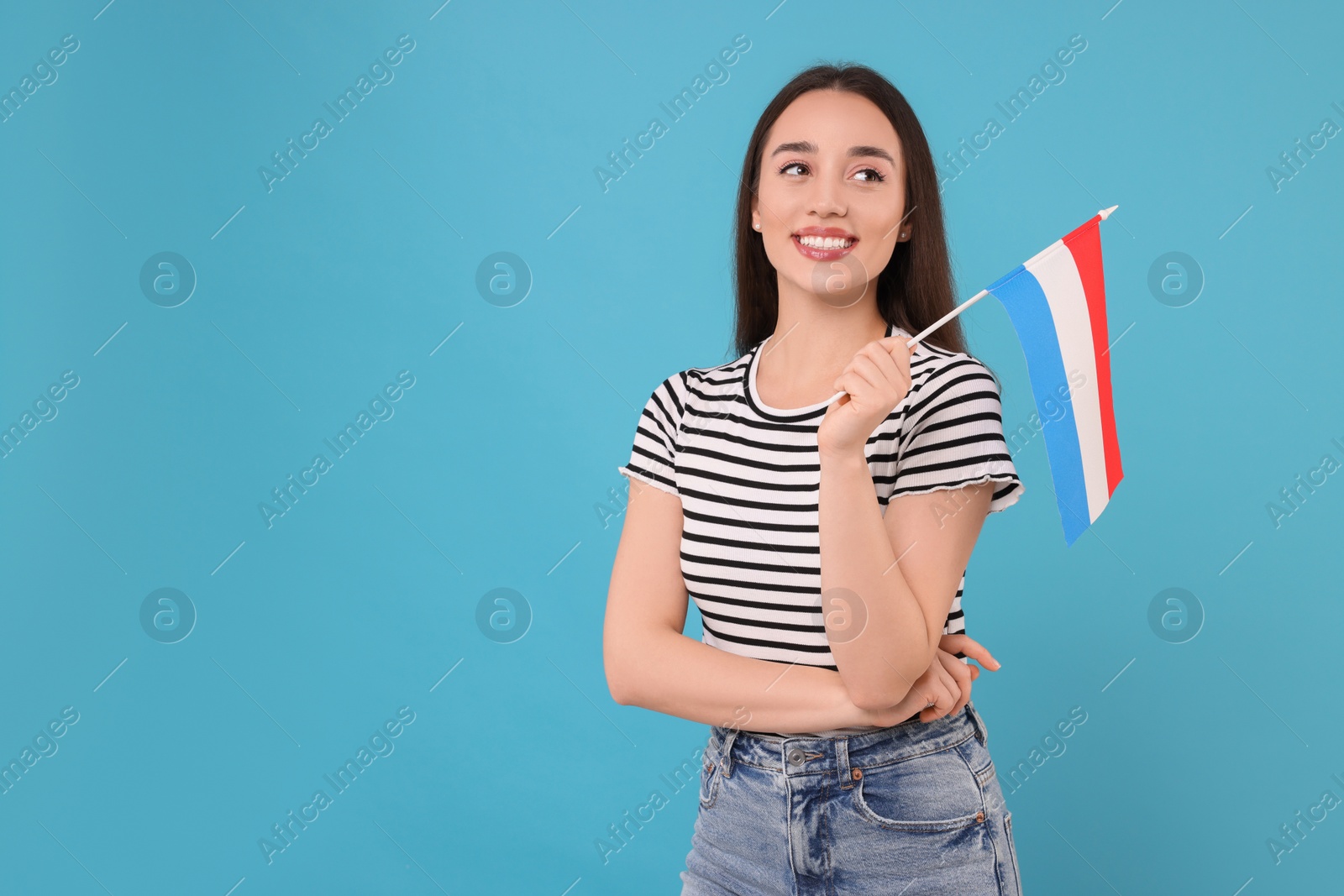 Photo of Young woman holding flag of Netherlands on light blue background, space for text