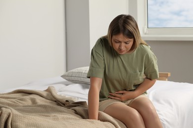 Photo of Young woman suffering from menstrual pain on bed at home, space for text
