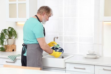 Photo of Senior man in protective gloves washing plate above sink in kitchen