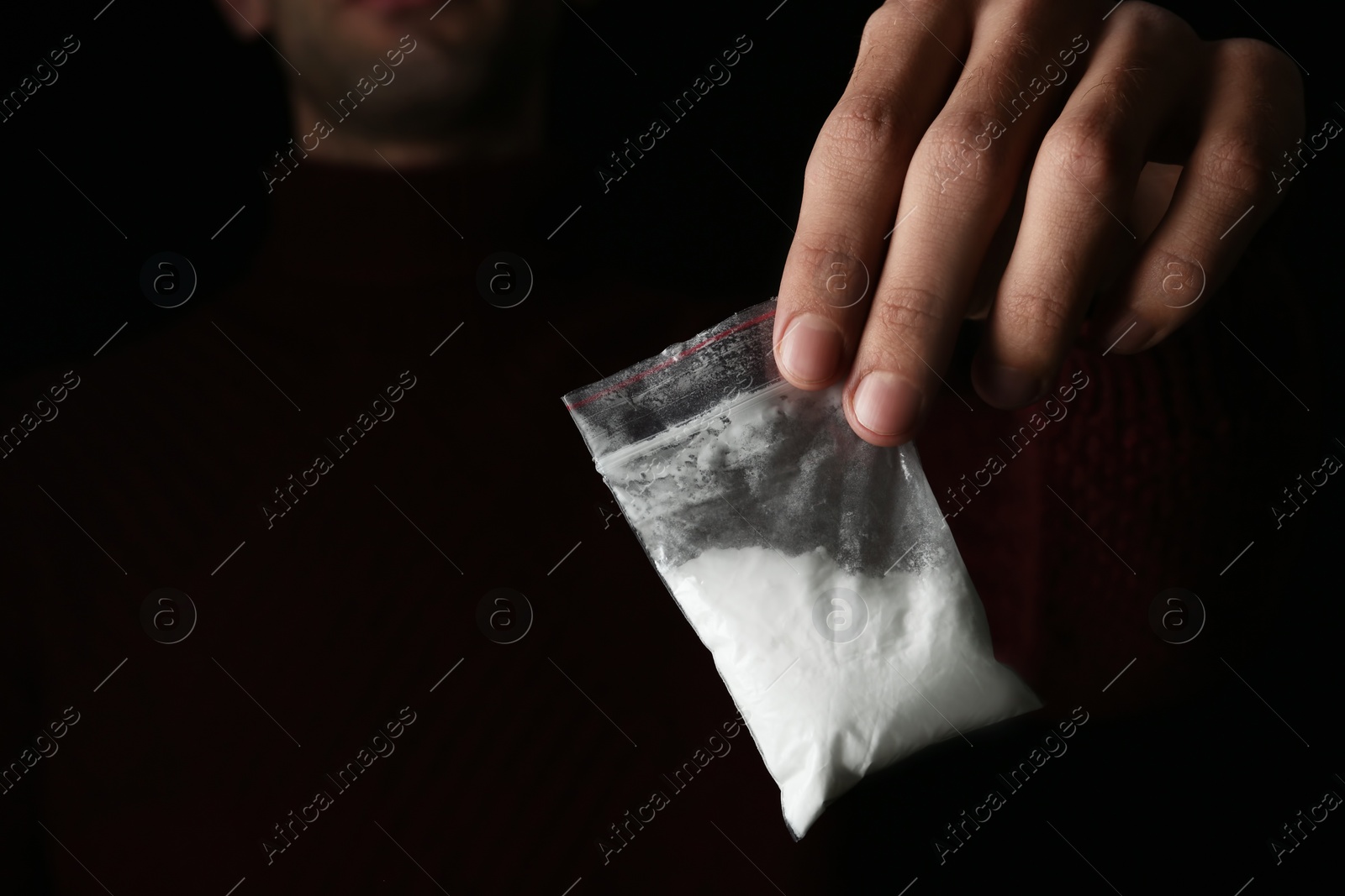 Photo of Drug dealer holding bag with cocaine on black background, closeup. Space for text