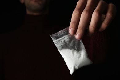 Photo of Drug dealer holding bag with cocaine on black background, closeup. Space for text