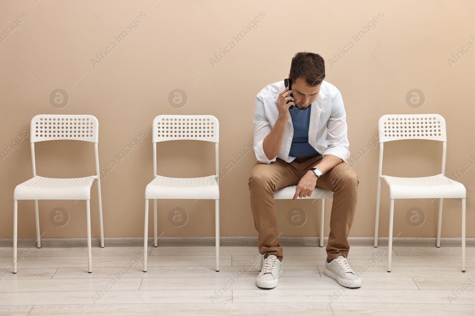 Photo of Man talking on smartphone and waiting for appointment indoors