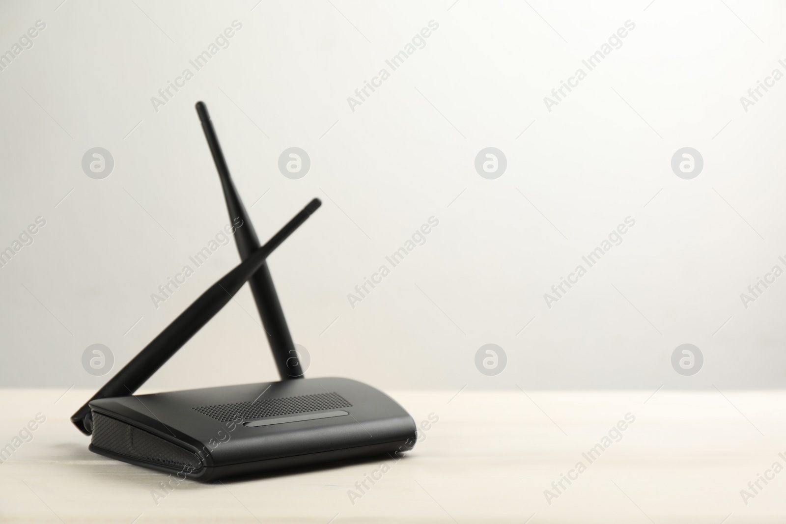 Photo of Modern Wi-Fi router on white wooden table against light background. Space for text