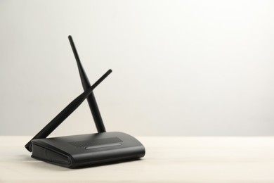 Modern Wi-Fi router on white wooden table against light background. Space for text