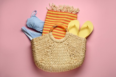 Beach bag with towel, swimsuit and flip flops on pink background, top view
