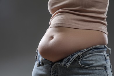 Woman with excessive belly fat on grey background, closeup. Overweight problem