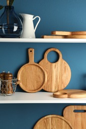 Photo of Wooden cutting boards and kitchen utensils on shelving unit near blue wall