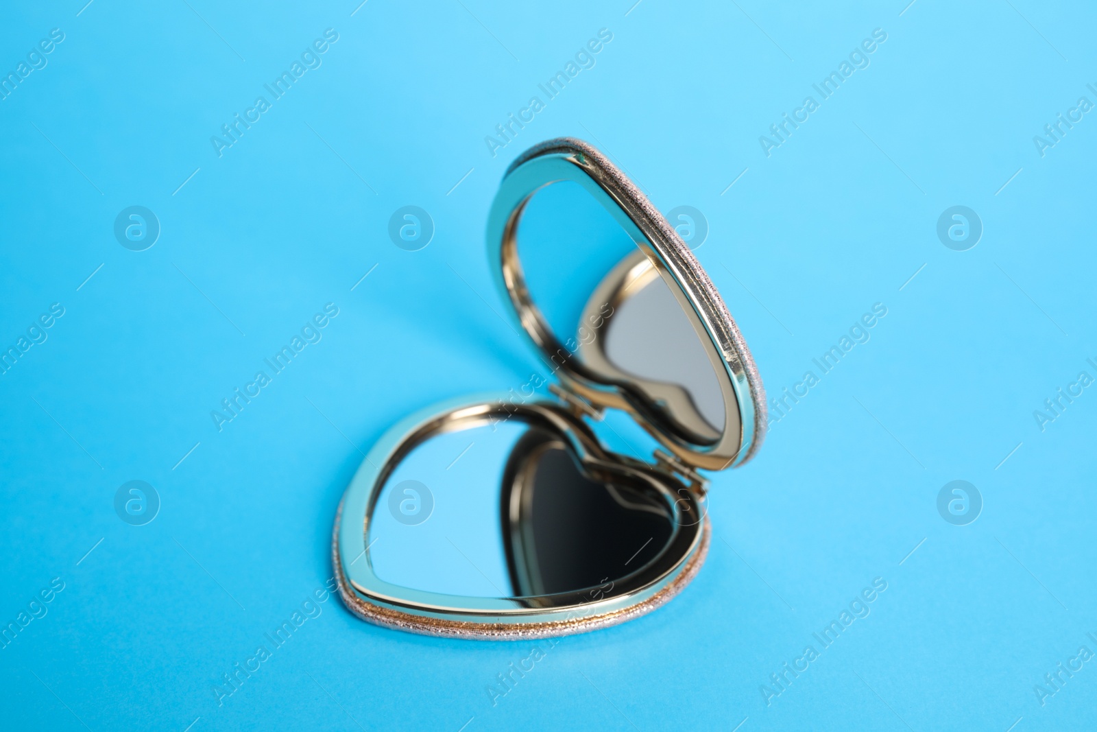 Photo of Stylish heart shaped cosmetic pocket mirror on light blue background