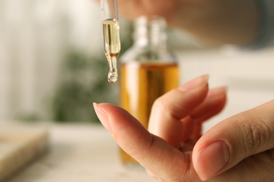 Photo of Woman dripping essential oil on finger at table, closeup