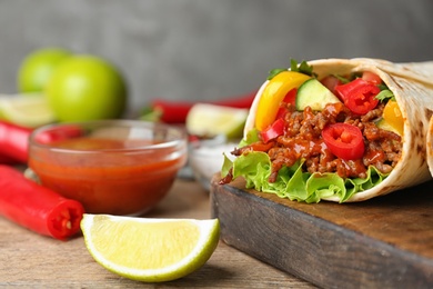 Photo of Board with delicious meat tortilla wrap on wooden table, closeup