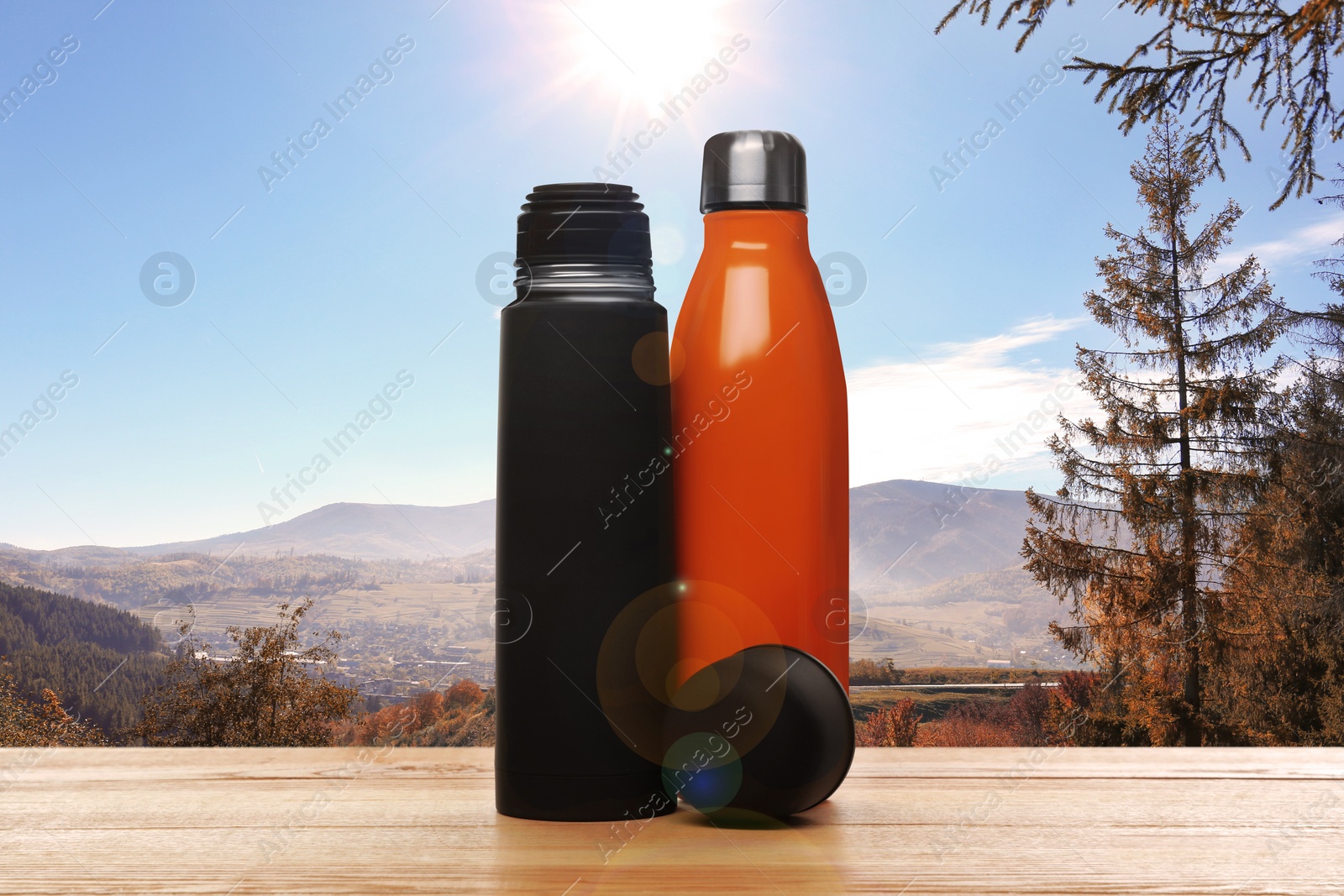Image of Wooden desk with thermo bottles and mountain landscape on background