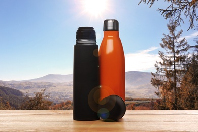 Wooden desk with thermo bottles and mountain landscape on background