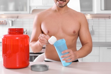 Photo of Young shirtless man preparing protein shake at table in kitchen, closeup