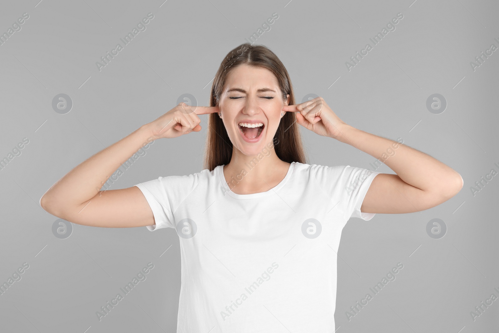 Photo of Emotional young woman covering her ears with fingers on grey background