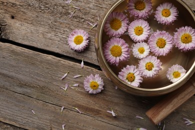 Photo of Tibetan singing bowl with water, chrysanthemum flowers and mallet on wooden table, flat lay. Space for text