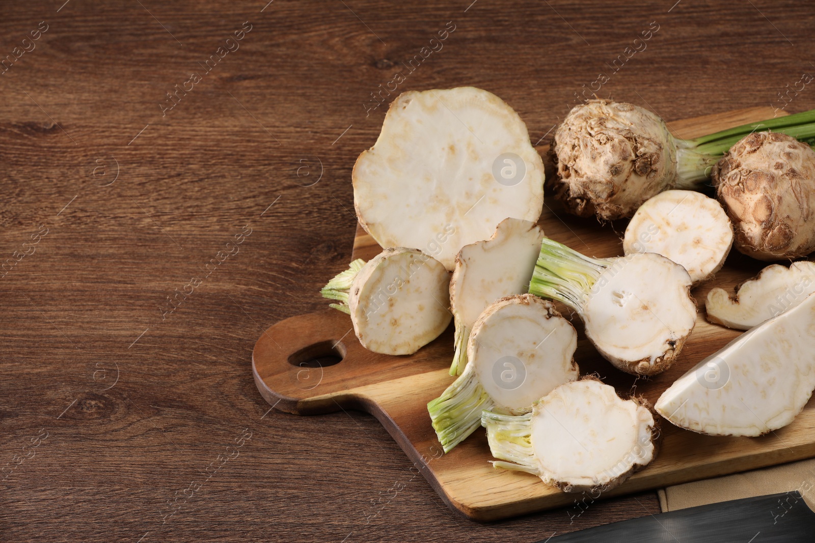 Photo of Whole and cut celery roots on wooden table, space for text