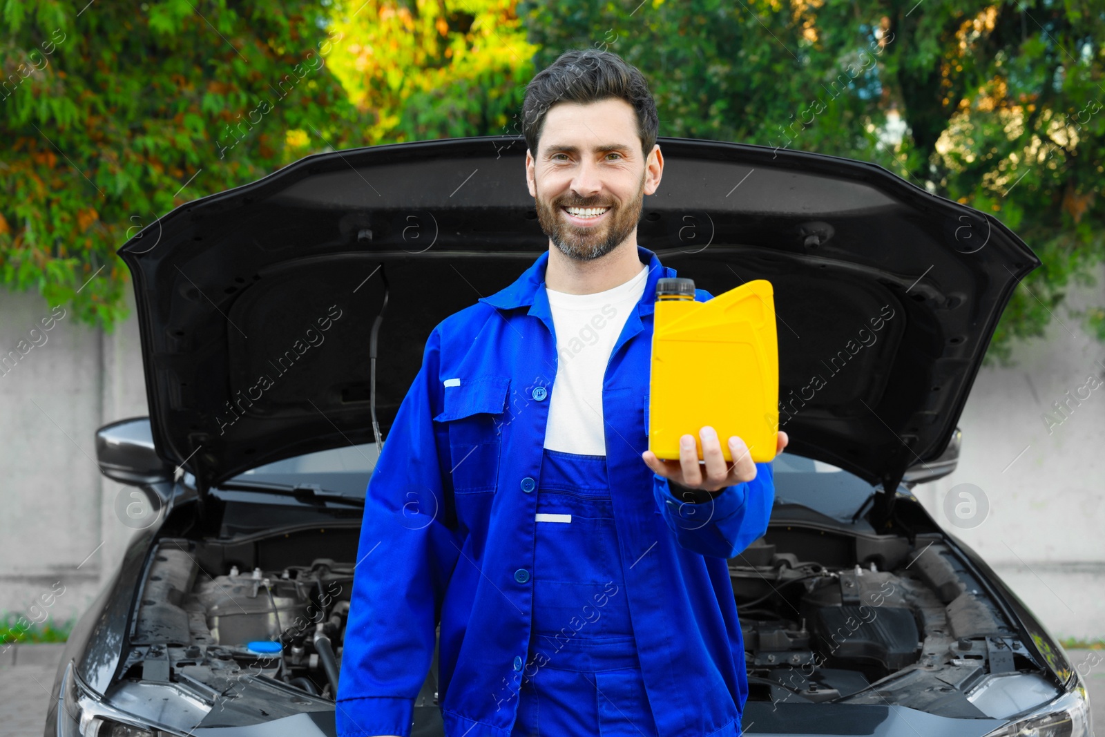 Photo of Smiling worker holding yellow container of motor oil near modern car