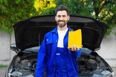 Photo of Smiling worker holding yellow containermotor oil near modern car