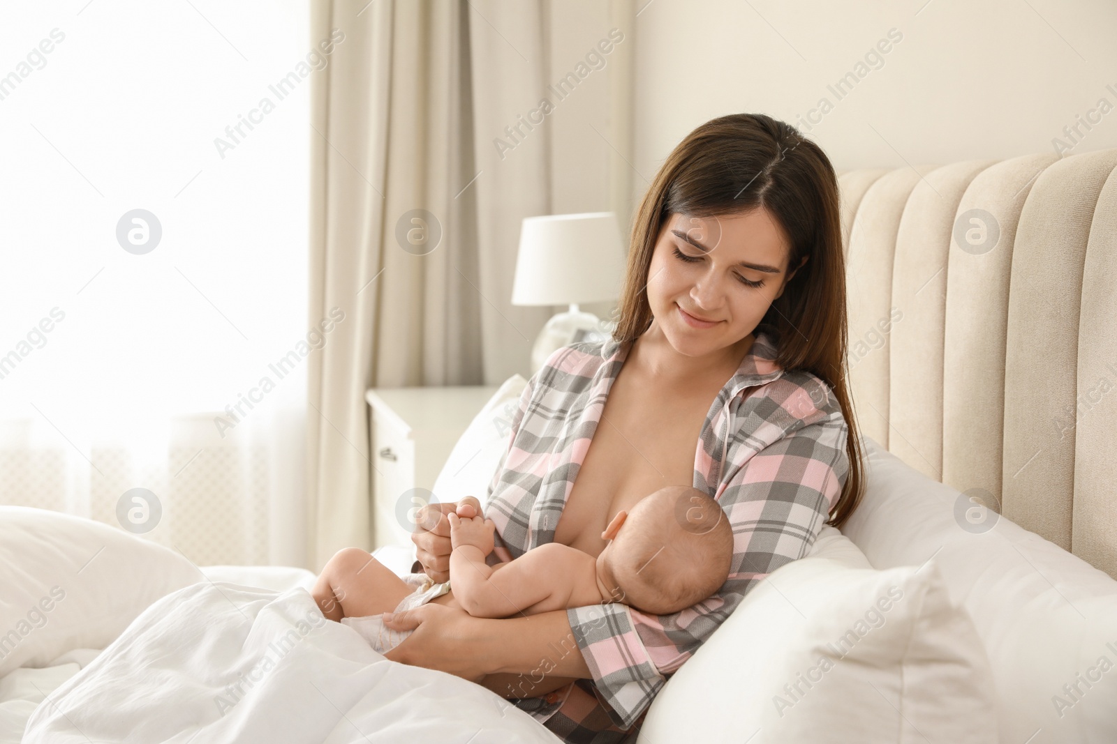 Photo of Young woman breastfeeding her little baby on bed at home