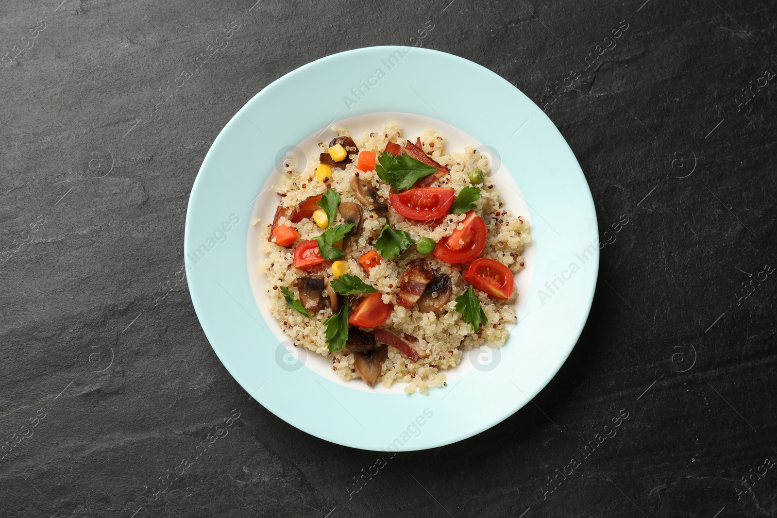 Photo of Plate of tasty quinoa porridge with fried bacon, mushrooms and vegetables on black table, top view