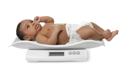 Photo of African-American baby lying on scales against white background