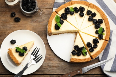 Photo of Sliced delicious cheesecake with blackberries on wooden background, flat lay