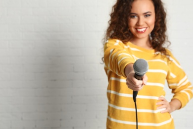 Curly African-American woman in sweater holding microphone near brick wall. Space for text