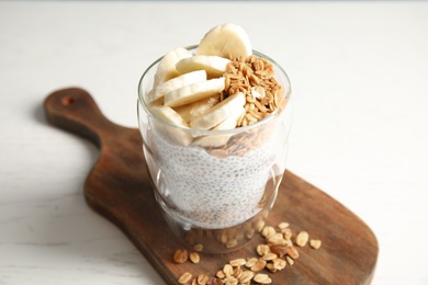 Glass of tasty chia seed pudding with banana and granola served on table