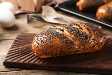 Photo of Board with freshly baked poppy seed roll on table