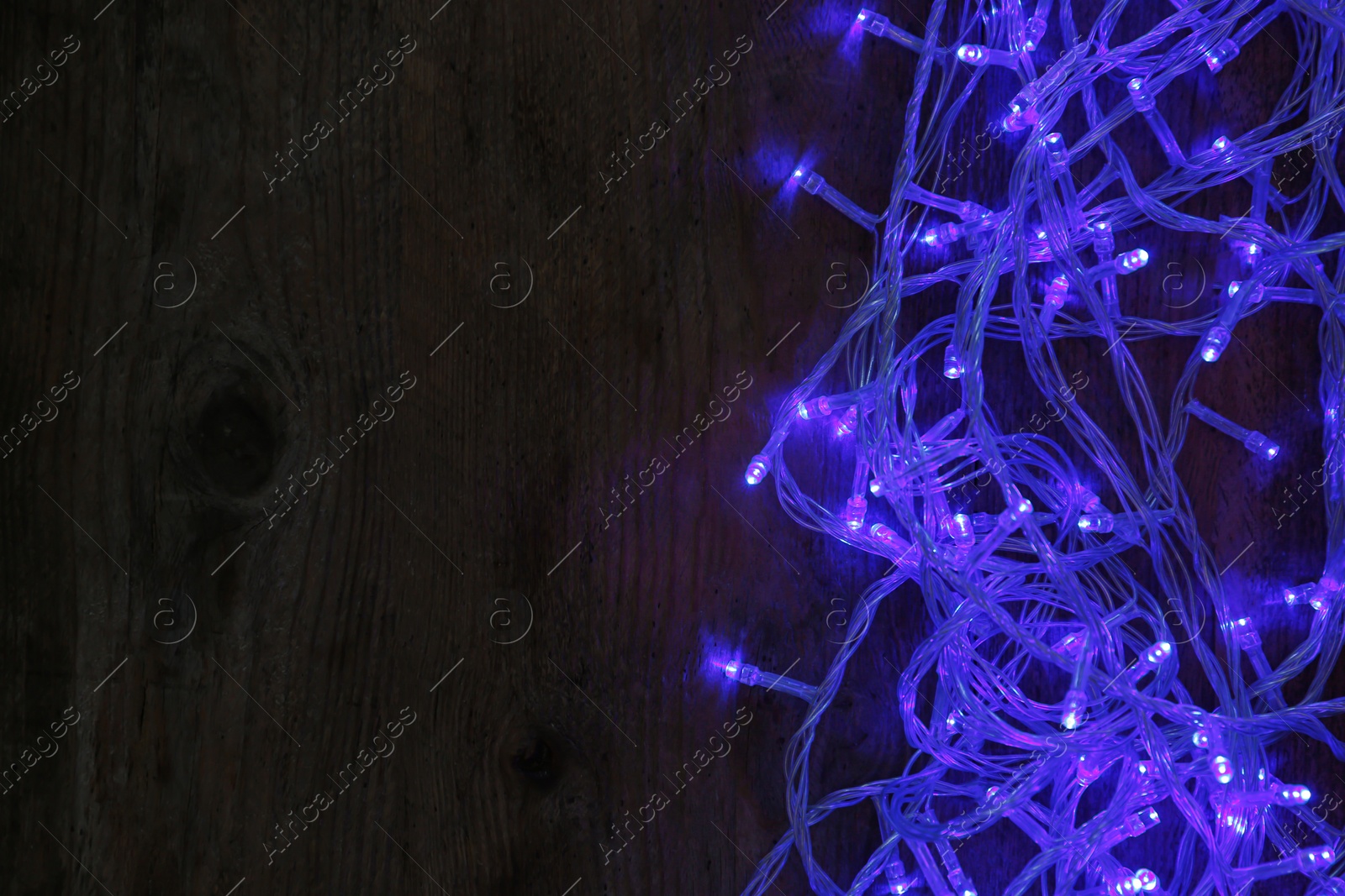 Photo of Blue Christmas lights on wooden background, top view. Space for text