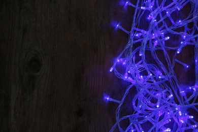 Photo of Blue Christmas lights on wooden background, top view. Space for text