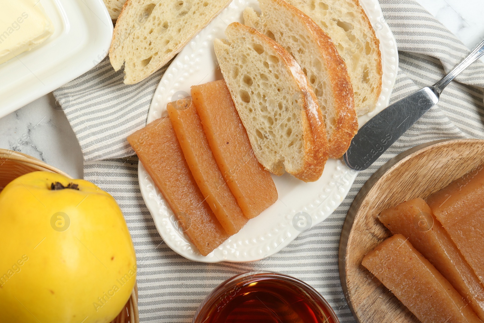 Photo of Delicious quince paste, bread, butter, cup of tea and fresh fruit on white marble table, flat lay