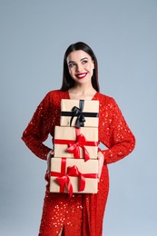 Woman in red dress holding Christmas gifts on grey background