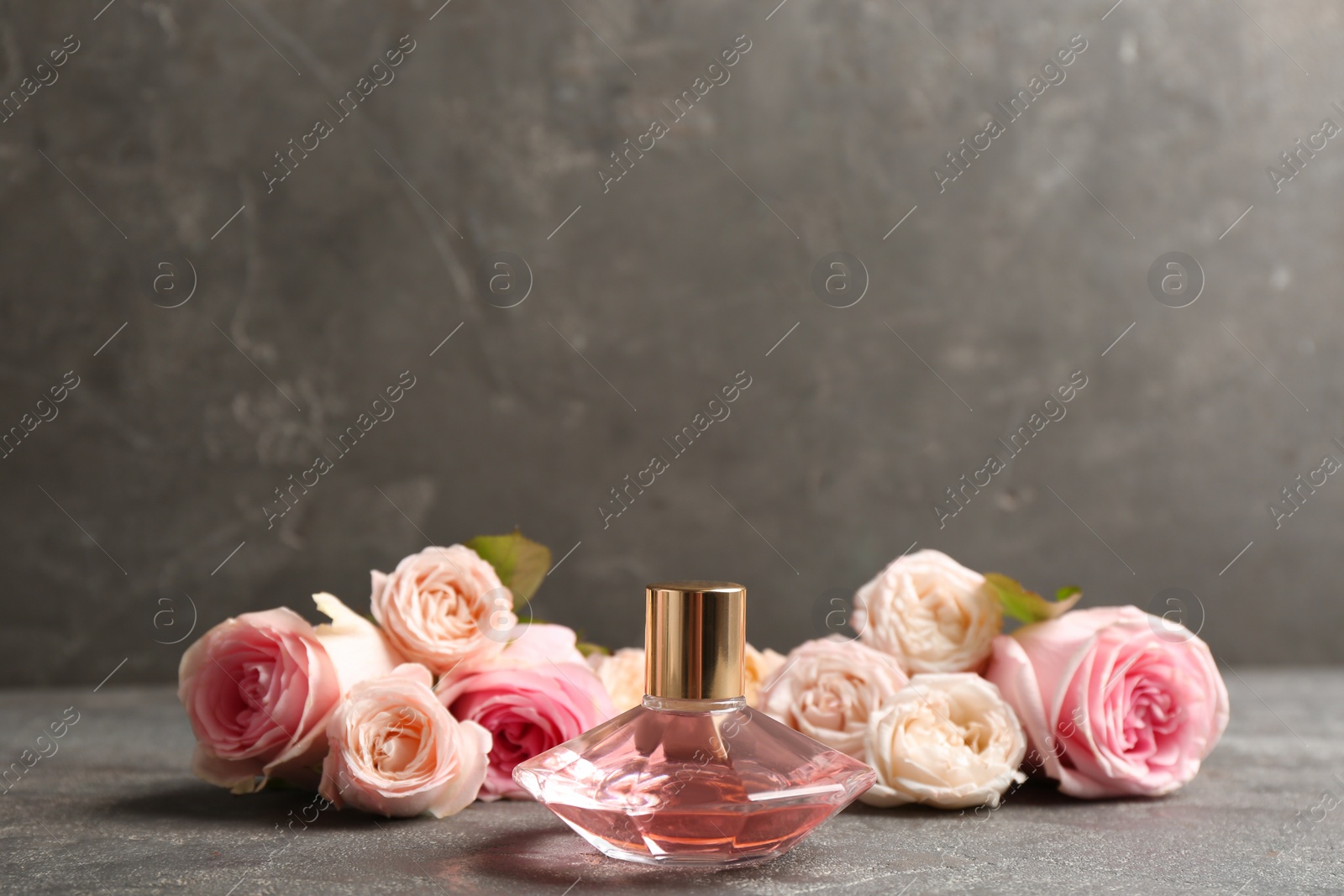 Photo of Bottle of perfume with beautiful roses on table. Space for text