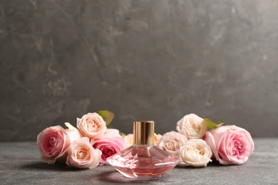 Bottle of perfume with beautiful roses on table. Space for text