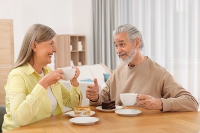 Affectionate senior couple having breakfast at wooden table in room
