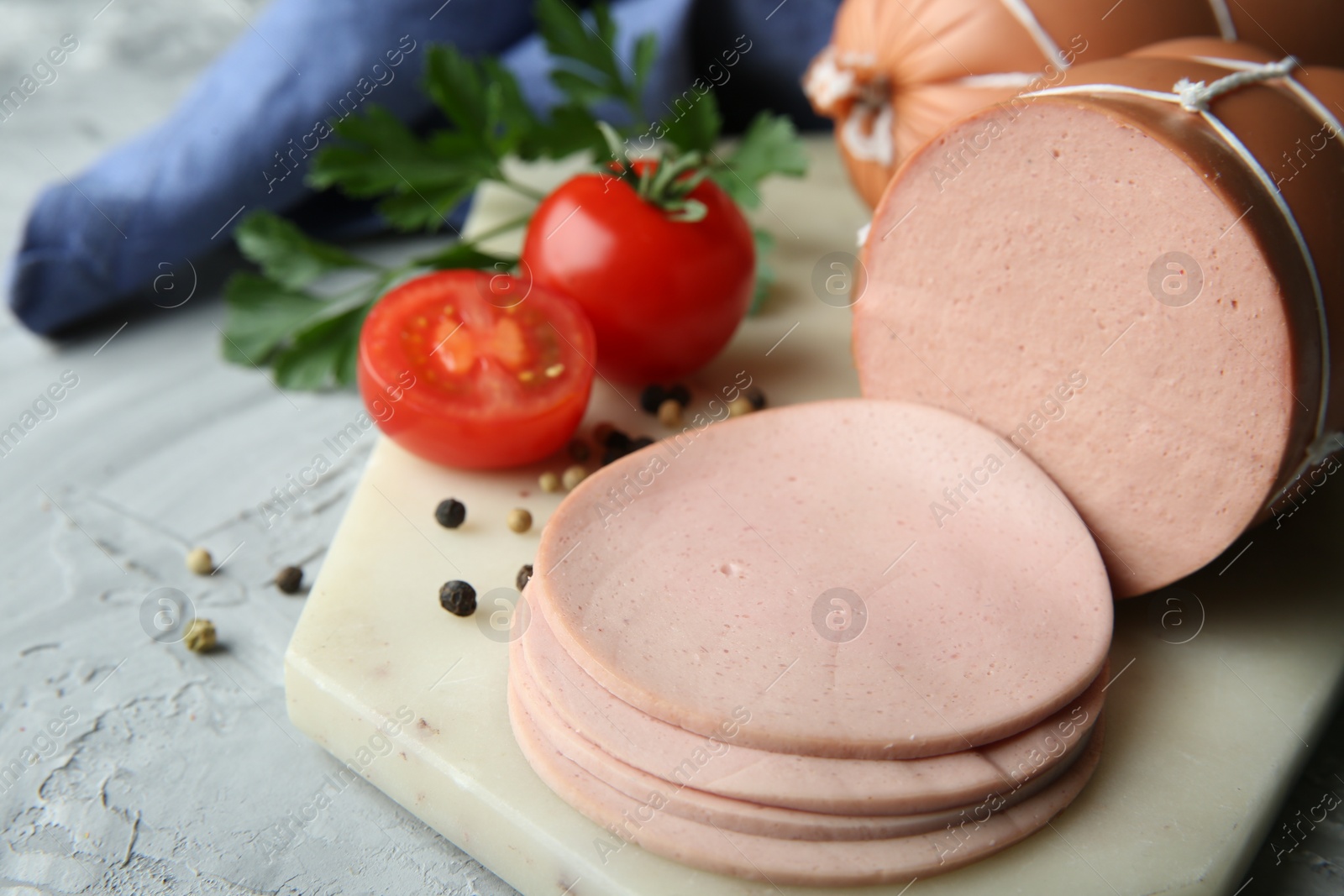 Photo of Delicious boiled sausage with tomatoes, parsley and spices on grey textured table, closeup