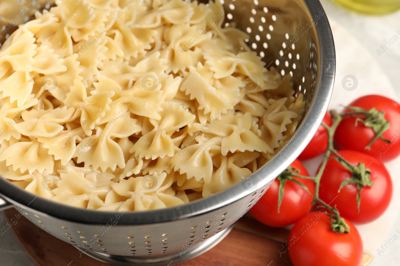 Photo of Cooked pasta in metal colander and tomatoes on table, closeup