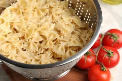 Cooked pasta in metal colander and tomatoes on table, closeup