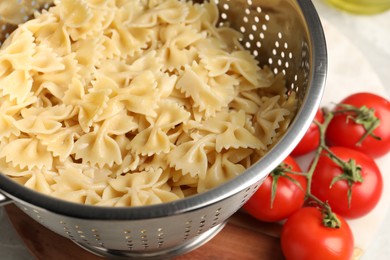 Photo of Cooked pasta in metal colander and tomatoes on table, closeup