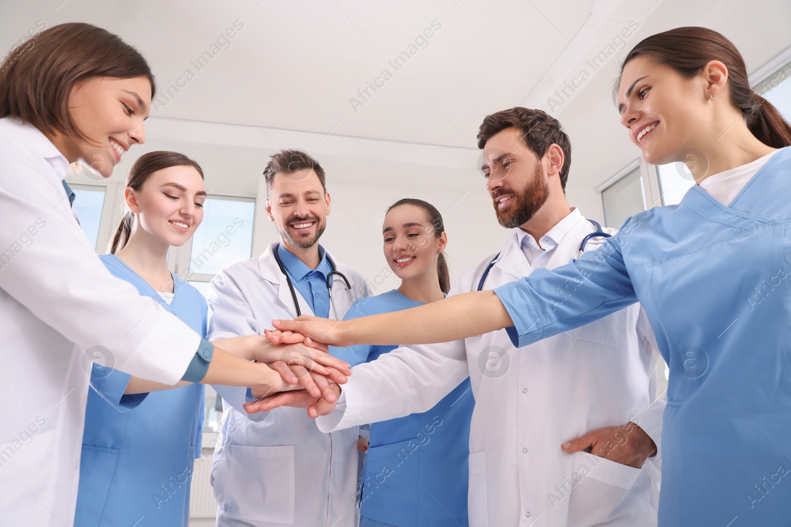Photo of Team of medical doctors putting hands together indoors