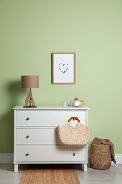 Modern white chest of drawers with lamp and decor near light green wall indoors